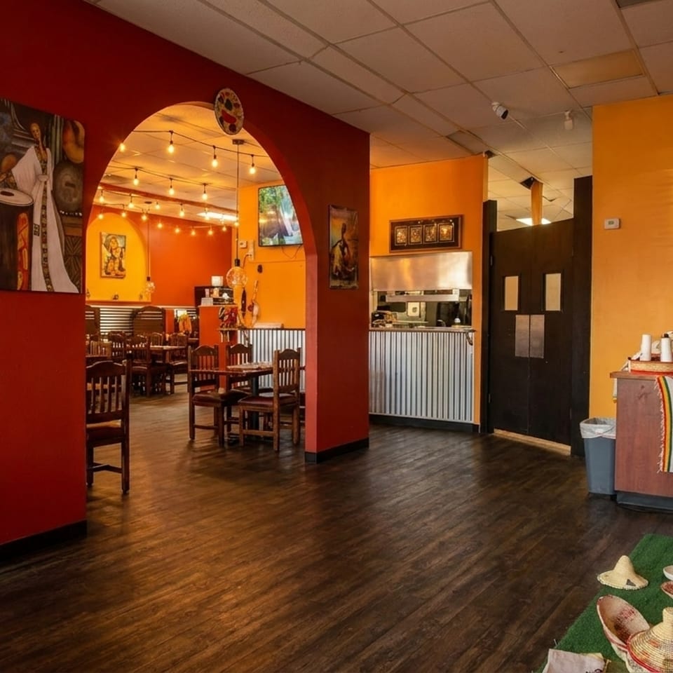 Vibrant restaurant interior with red arched doorways, orange walls, dark wood floors, and cultural artwork.