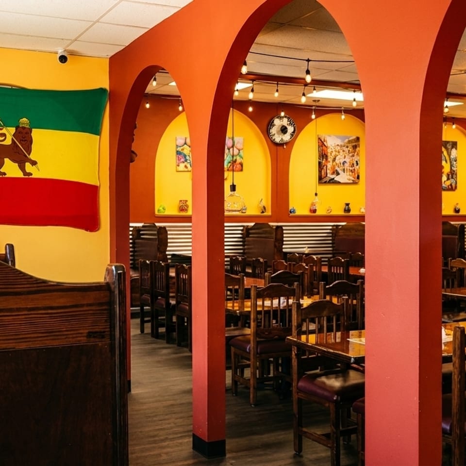 Restaurant interior with a large Ethiopian flag, orange archways, and wooden tables and chairs.