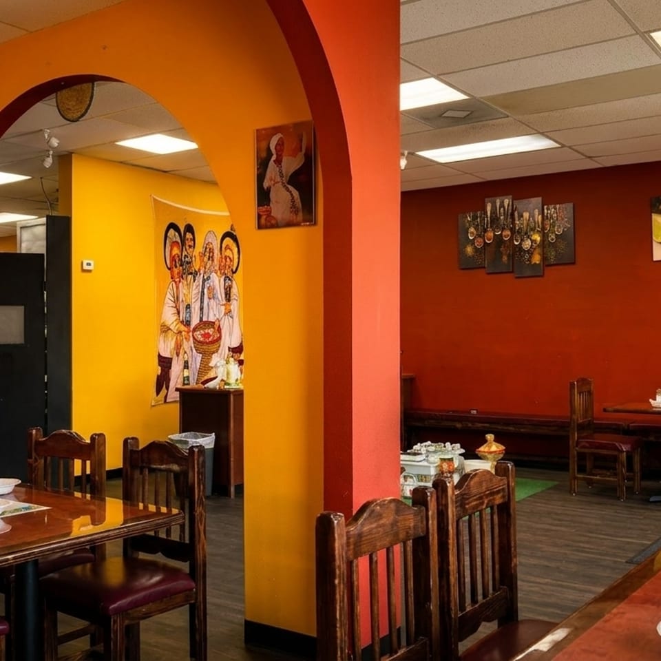Restaurant interior with colorful orange and red walls, wooden tables, chairs, and Ethiopian art.